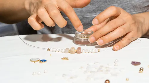 Hands crafting jewelry on a white table.