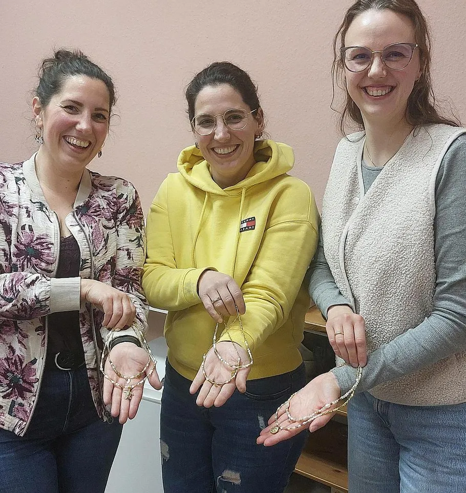 Drei Frauen lächeln, halten Schmuckstücke drinnen.
