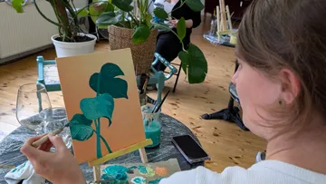 Person painting green leaves on canvas indoors.