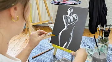 Woman painting a silhouette on black canvas.