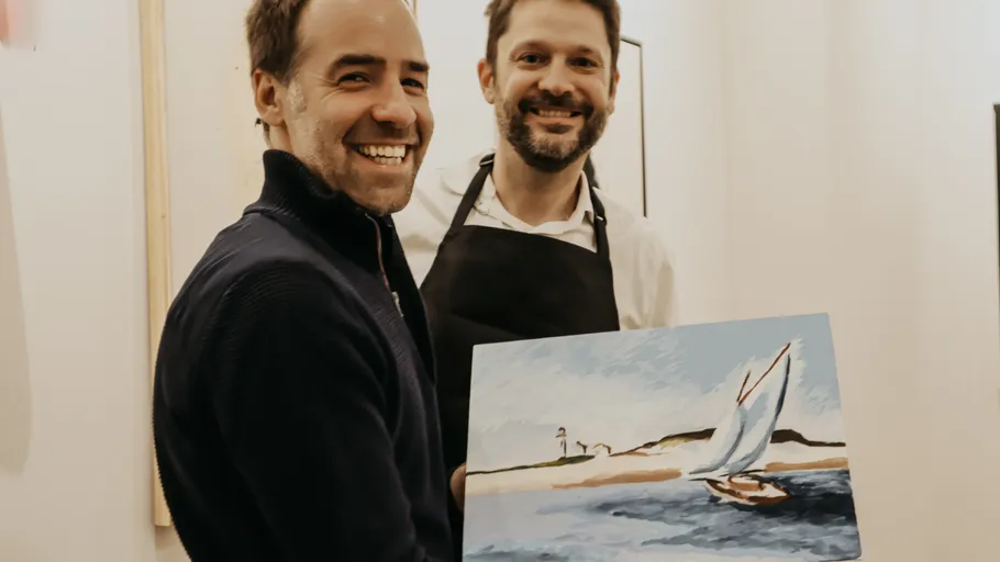 Zwei Männer lächeln, halten ein Segelbootgemälde.