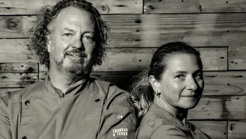 Two chefs standing in front of wooden wall.