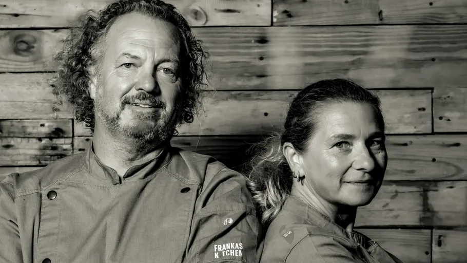 Two chefs standing in front of wooden wall.