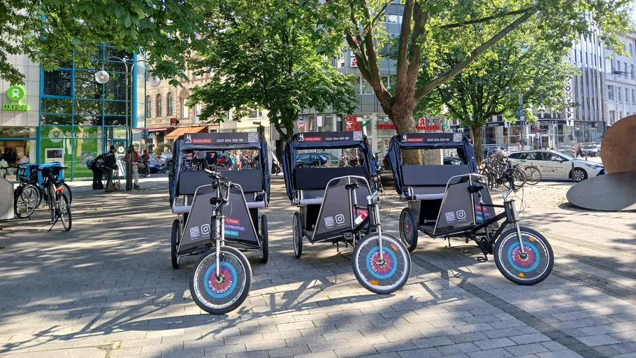 Drei Rikscha unter Bäumen in einer Stadt geparkt.