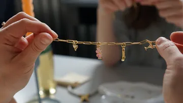 Hands holding charm bracelet over table.