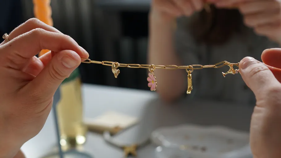 Hände halten Armband mit Anhängern über Tisch.