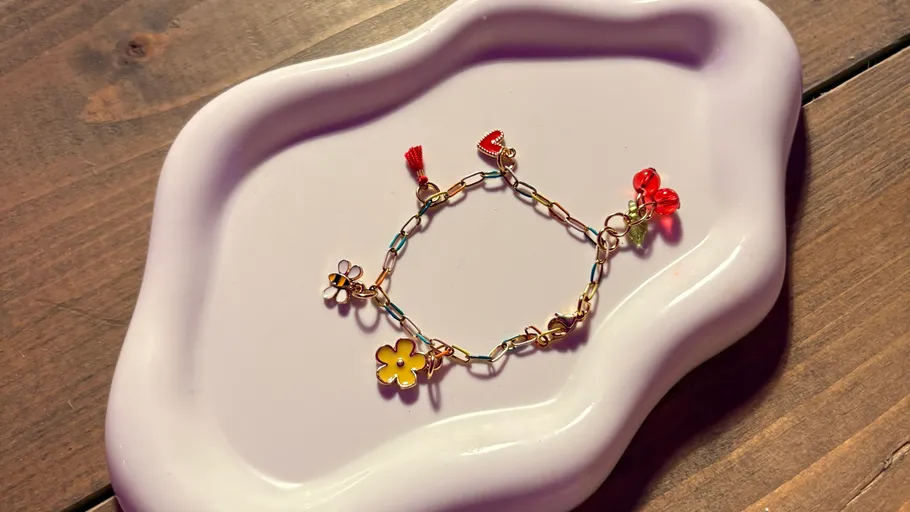 Armband mit Anhängern auf dekorativem Teller, Holztisch.