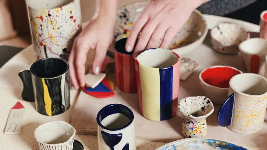 Hands arranging colorful ceramic mugs on table.