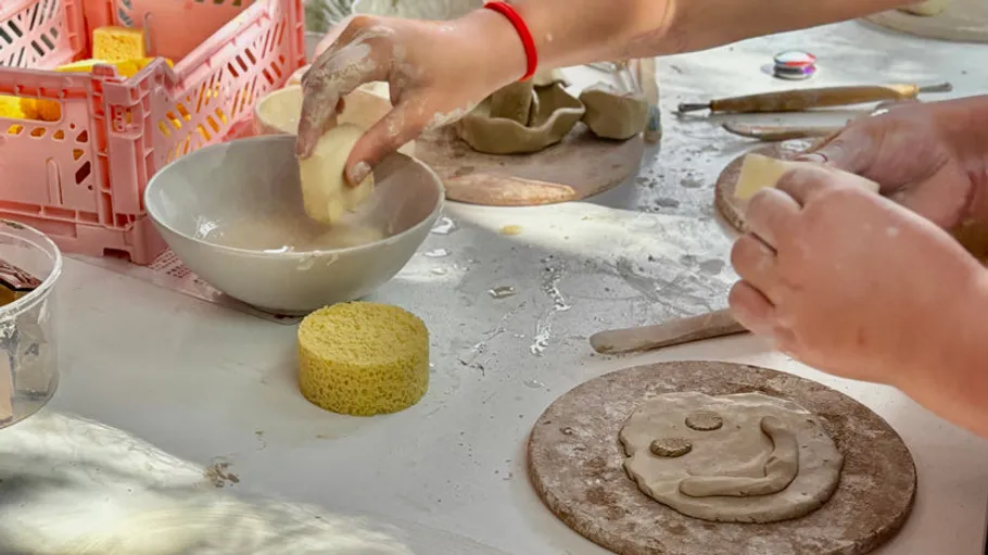 Hands crafting clay with tools and bowls nearby.