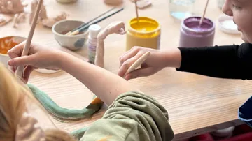 Children painting clay figures at a table.