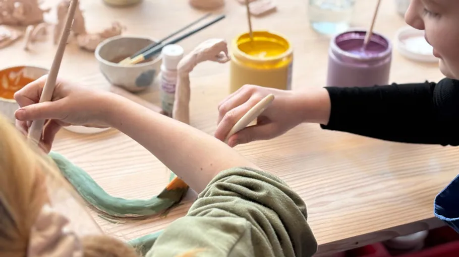 Children painting clay figures at a table.