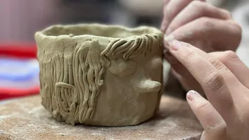 Hands shape clay into textured cup design.
