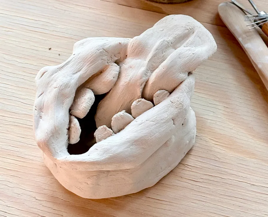 Clay sculpture of a hand on wood table.