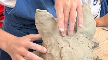 Hände formen Tonskulptur in Werkstatt.