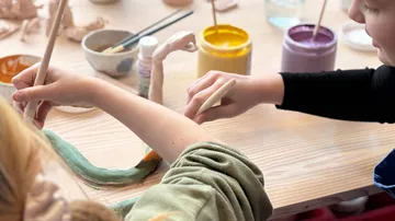 Hände bemalen Tonskulpturen auf einem Tisch.