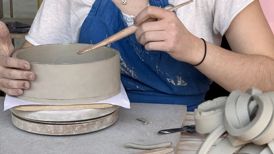 Person crafting pottery bowl with tool, studio setting.