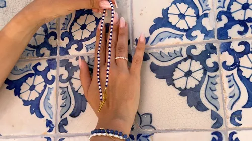 Hände mit Schmuck vor blauen Fliesen.