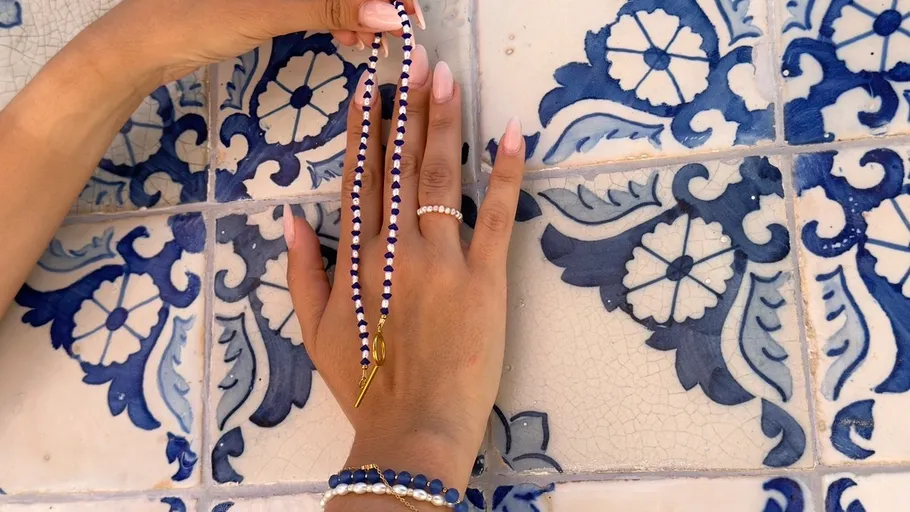 Hände mit Schmuck vor blauen Fliesen.