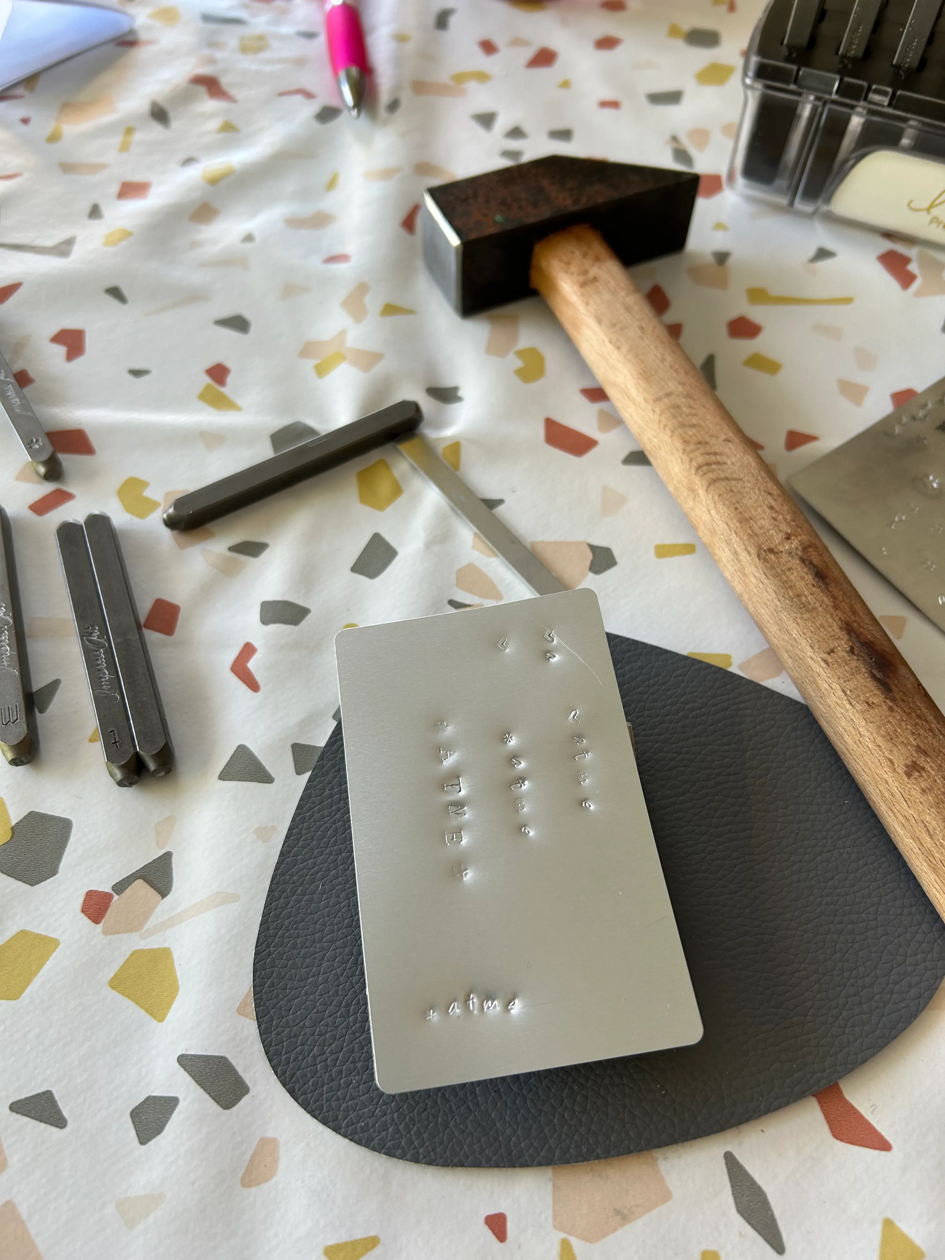Metallplatte, Hammer und Stempel auf Tischdecke.