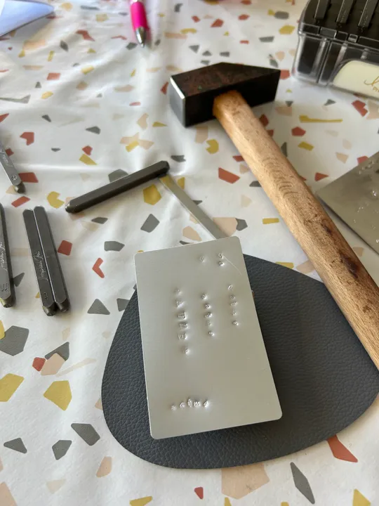 Metallplatte, Hammer und Stempel auf Tischdecke.