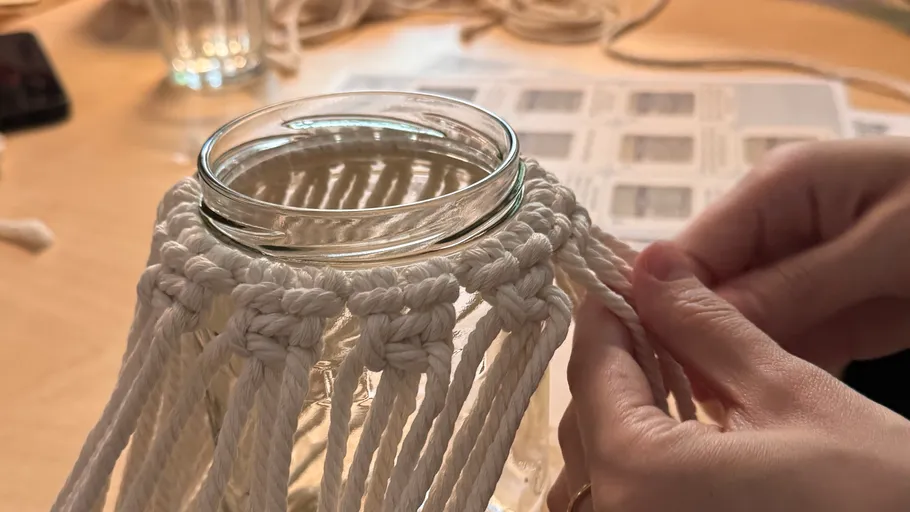 Hands crafting macramé on a glass jar.