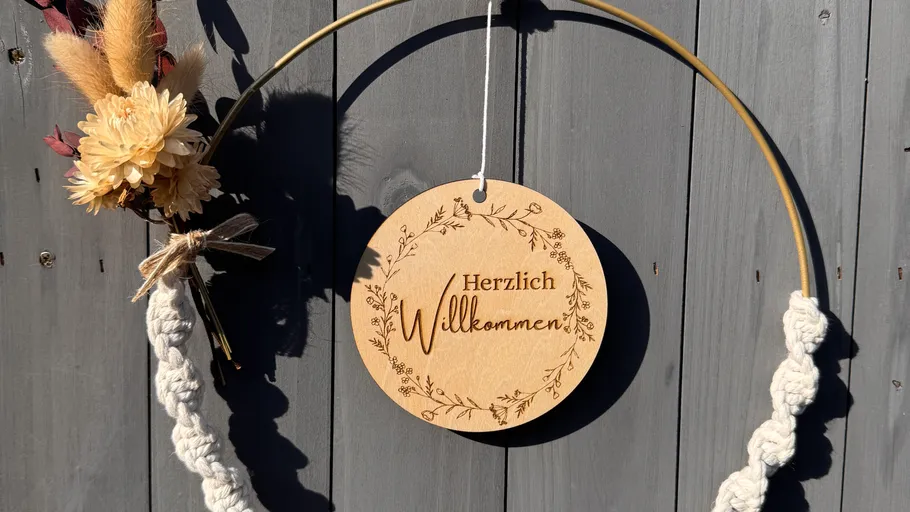 Kranz mit Blumen und Willkommensschild, Holzuntergrund.