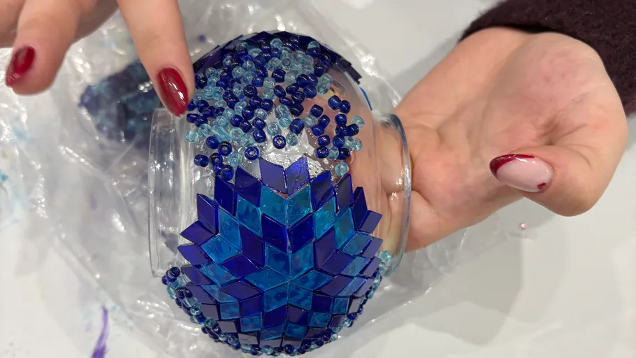 Hände halten eine verzierte blaue Glasschale.