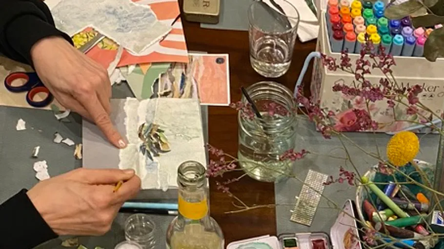 Hands creating collage, surrounded by art supplies.