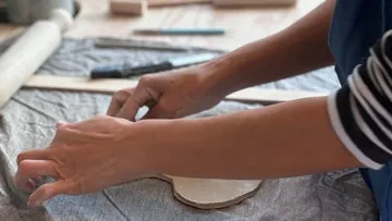 Hands shaping clay on a table surface.