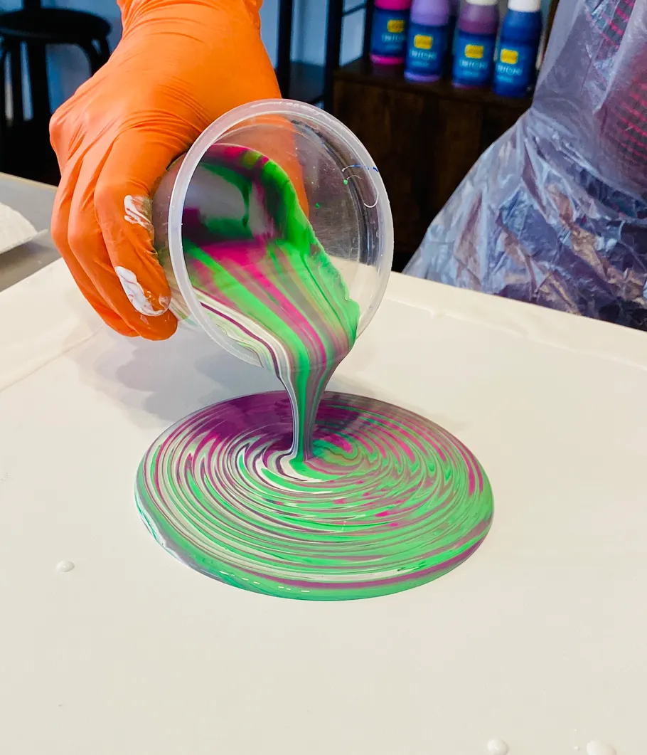 Hand pouring colorful paint on canvas.