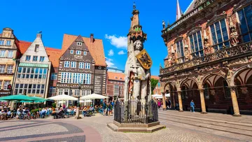 Statue in city square with historic buildings.