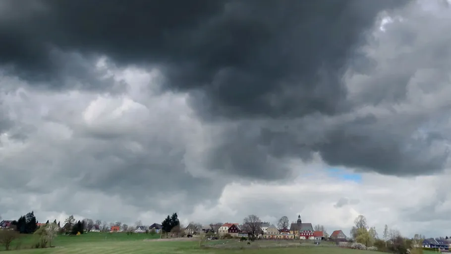 Dunkle Wolken über ländlicher Dorflandschaft.