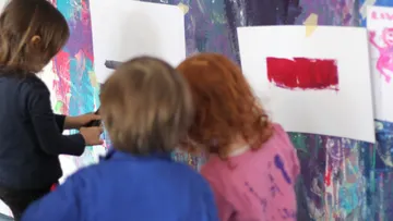 Kinder malen an einer bunten Wand.