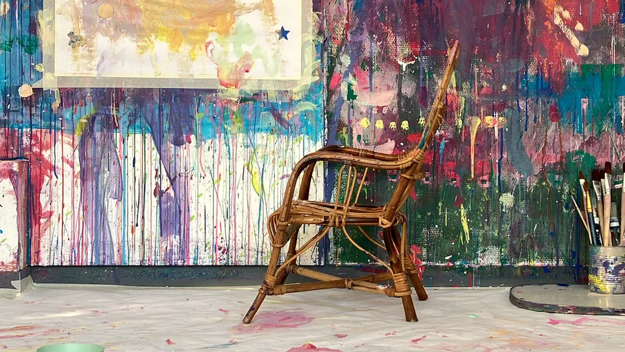 Wooden chair in colorful paint-splattered studio.