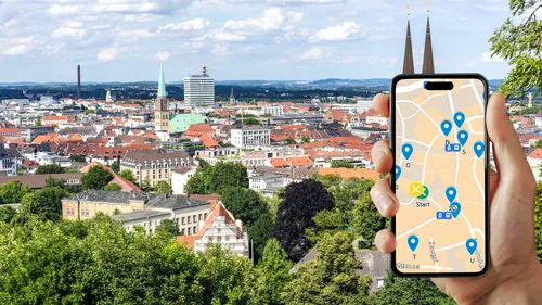 Hand hält Handy mit Karte, Stadtsilhouette im Hintergrund.