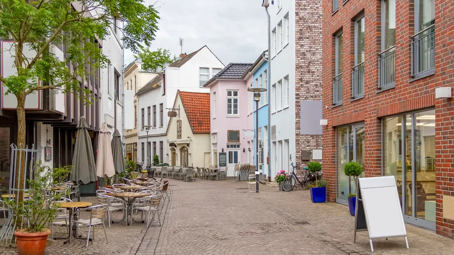 Gepflasterte Straße mit bunten Gebäuden und Cafés.