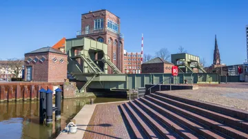 Brücke und Backsteingebäude am Kanal unter blauem Himmel.