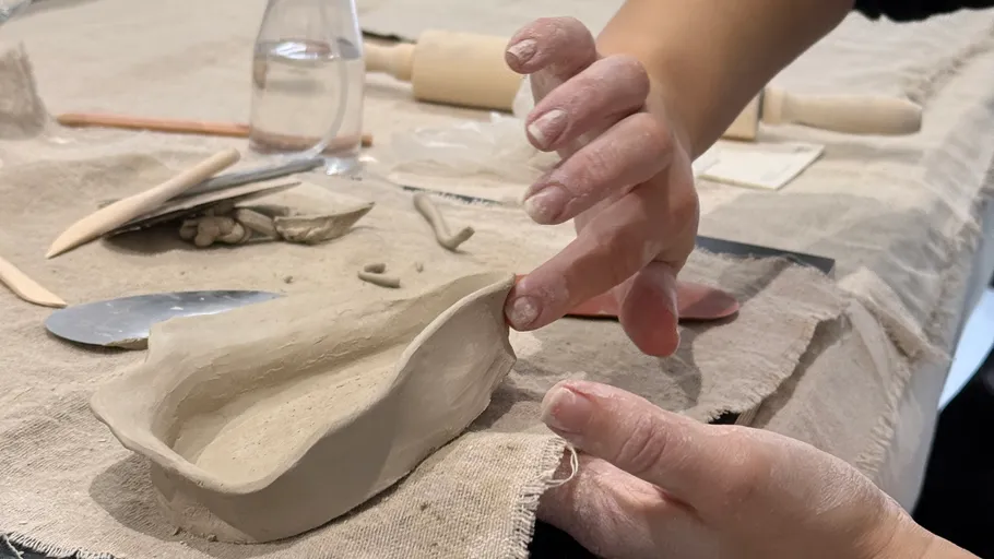 Hands shaping clay on a table.