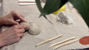 Hände formen Ton auf einer Tischdecke.
