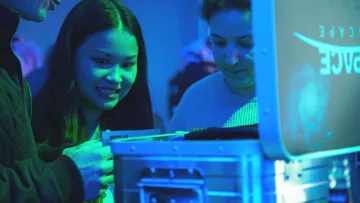 People examining object in blue-lit room.
