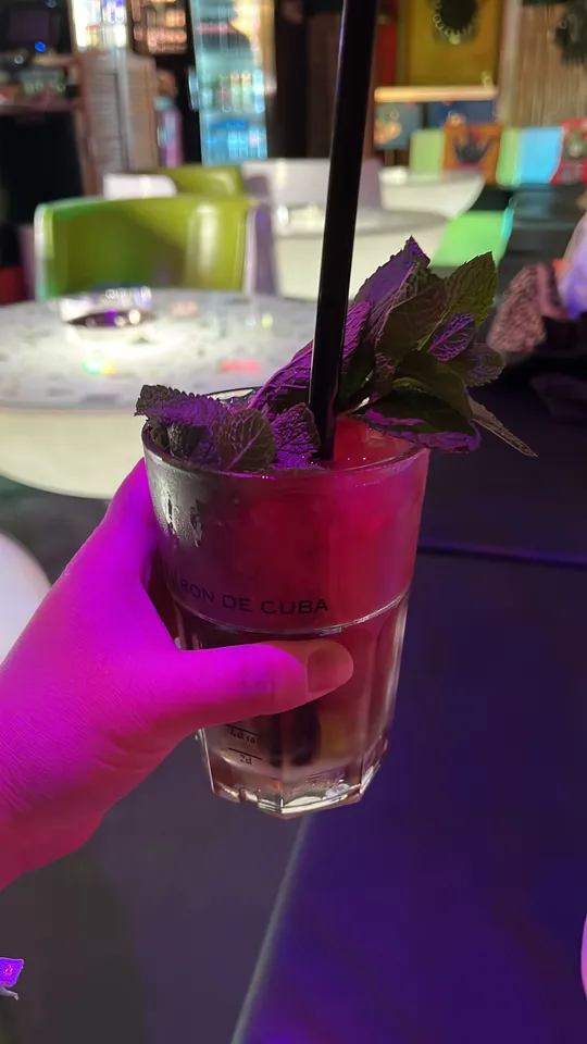Hand holding drink with mint in a bar.