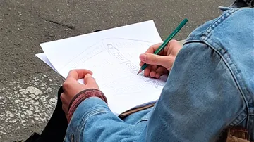 Person sketching a building on paper outdoors.