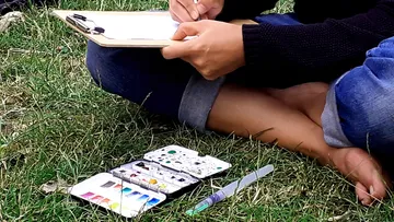 Person painting outdoors on the grass.