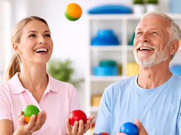 Two people happily juggling balls indoors.