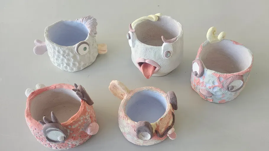 Five colorful, textured ceramic cups with quirky faces.