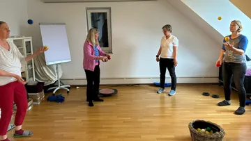 Four people juggle balls in a room.