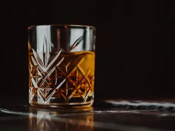 Glas mit Whisky steht auf einem dunklen Tisch.