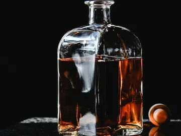 Eine Glasflasche enthält dunkelbraune Flüssigkeit vor schwarzem Hintergrund.