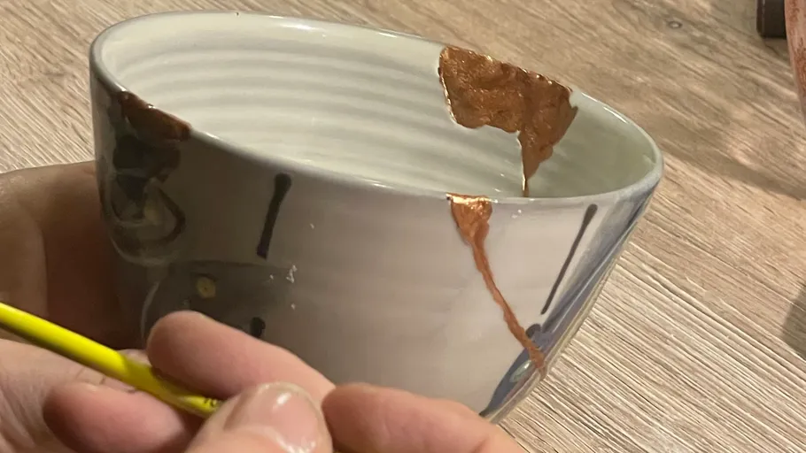Hand repairing bowl with gold, wooden surface.