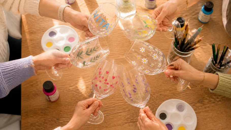 Hands holding decorated wine glasses around table.